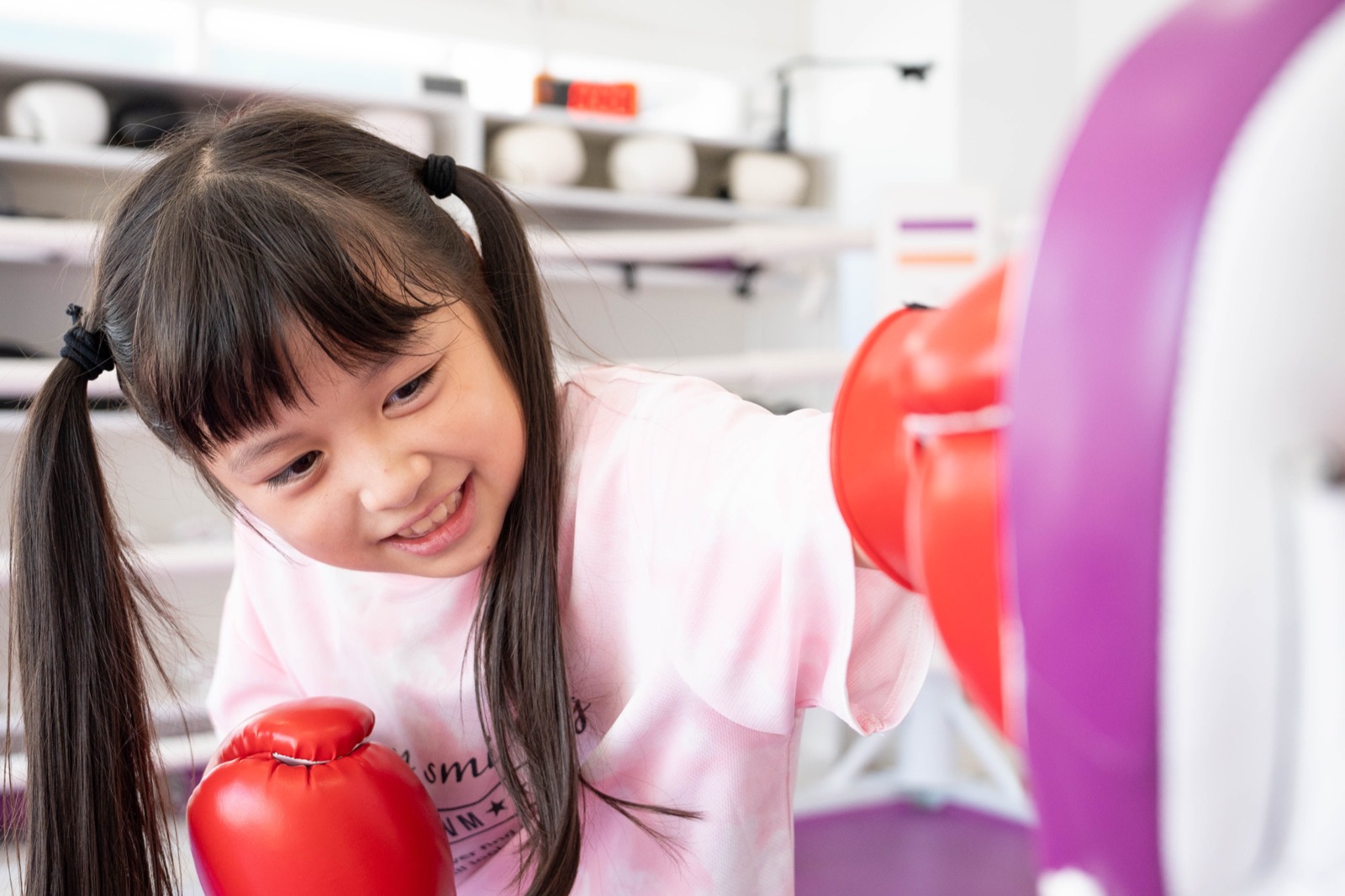 福岡 薬院の小学生英会話 English Fight Kidsのジムで、笑顔の小学生が明るい空間でミットにパンチし、奥で友達がラダーゲームをしているノンコンタクト指導風景